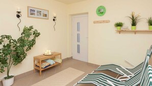 Una habitación con un banco de madera, una pequeña mesa con velas, una planta en maceta y un estante montado en la pared con plantas.