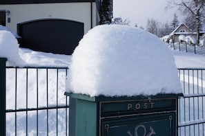 A snow-covered mailbox with the word 'POST' on it, a metal fence, and a garage door in the background.