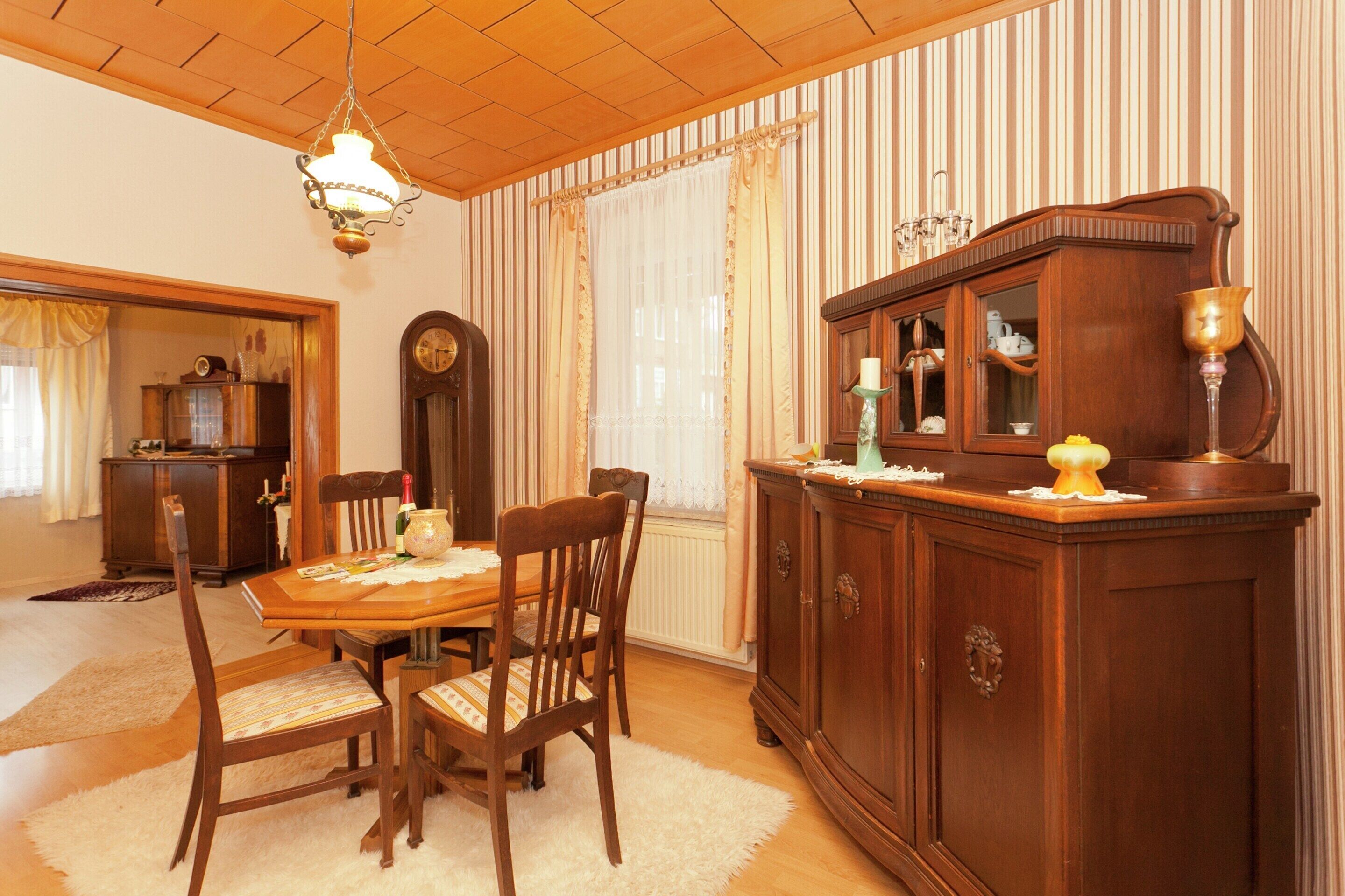 A dining area with a wooden table and chairs, a cabinet with glass doors, and a chandelier.