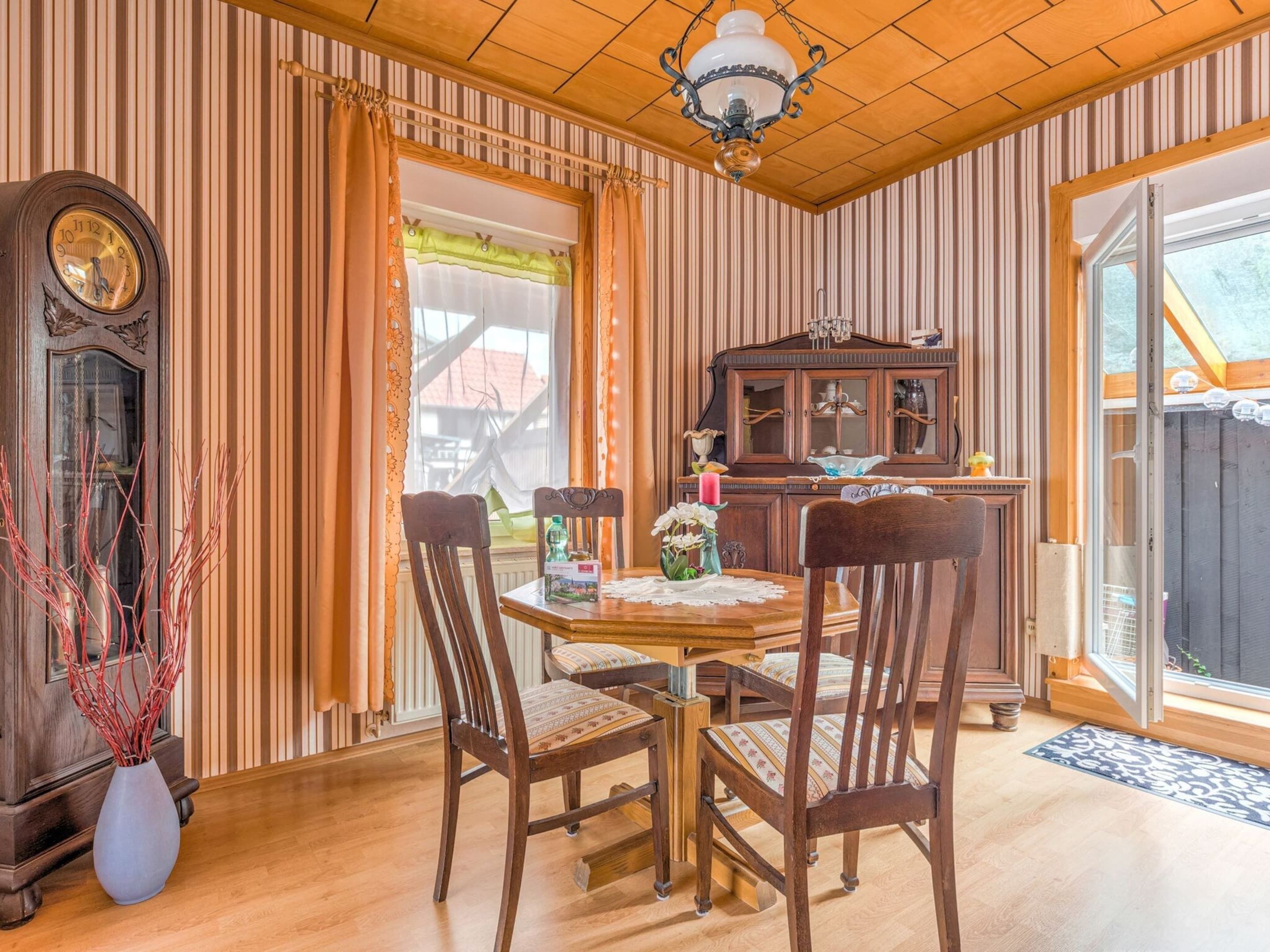 Un coin repas avec une table en bois, des chaises, une horloge et un buffet.