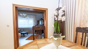 A dining area with a table set for two, a vase with white orchids, and a view into another room with a dining table and chairs.
