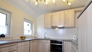 A modern kitchen with light wood cabinets, a stainless steel oven, and a window with a flower vase. - Graceful Apartment with Garden in Velmede near City Center (Bestwig)