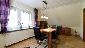 A dining area with a wooden table, four chairs, a chandelier, and a window with curtains. - Graceful Apartment with Garden in Velmede near City Center (Bestwig)