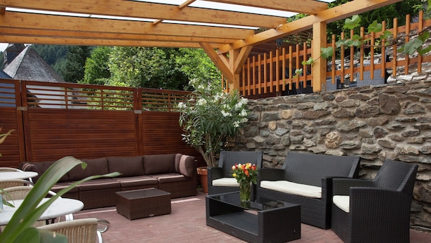 Un espace patio extérieur agrémenté d’un mur en pierre, d’une pergola en bois, de meubles en osier et d’une plante en pot.