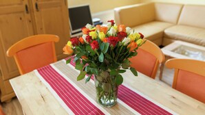 Une table à manger ornée d’un vase rempli de fleurs colorées, des chaises en bois, une nappe à rayures, un buffet en bois et un canapé en arrière-plan.