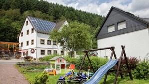Une aire de jeux avec un toboggan et une balançoire, entourée d’une pelouse et d’un bâtiment équipé de panneaux solaires.
