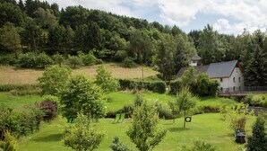 Une maison entourée d’un paysage verdoyant et luxuriant, avec une colline en arrière-plan.