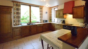 A kitchen with wooden cabinets, a window with curtains, a sink, a stove, and a table with a newspaper. - Spacious Retreat, Daverdisse (Daverdisse)