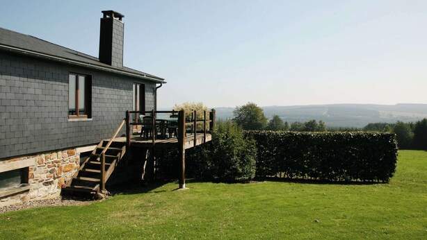 A house with a stone foundation, a grey brick exterior, and a wooden deck with a table and chairs. - Cozy Cottage, Basse-bodeux (Trois-Ponts)