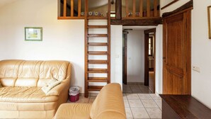 A living room with a high ceiling, a wooden staircase, a leather sofa, and a wooden door. - Cozy Cottage, Basse-bodeux (Trois-Ponts)