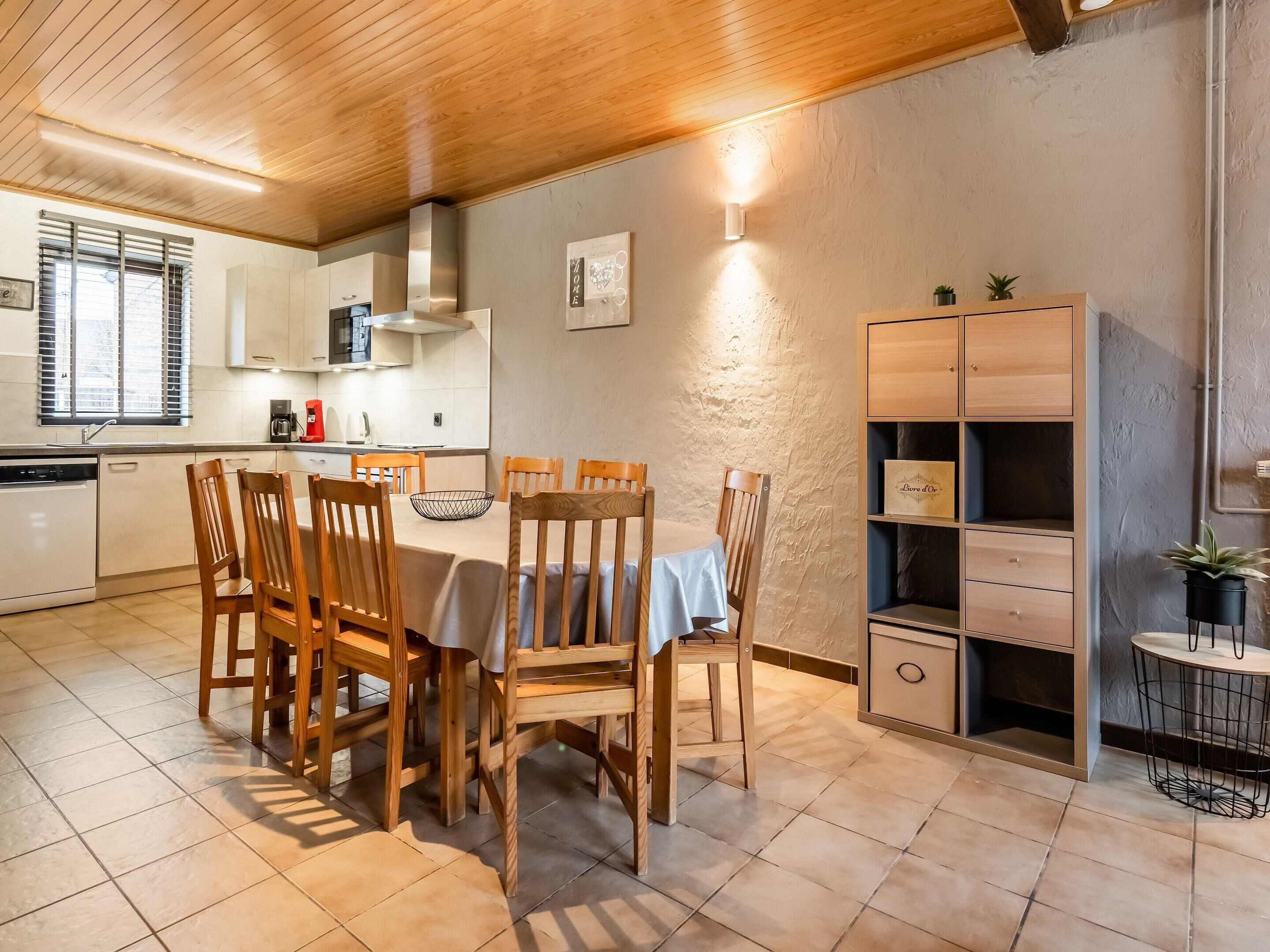 A dining area with a table and chairs, a kitchen in the background, and a built-in shelving unit.