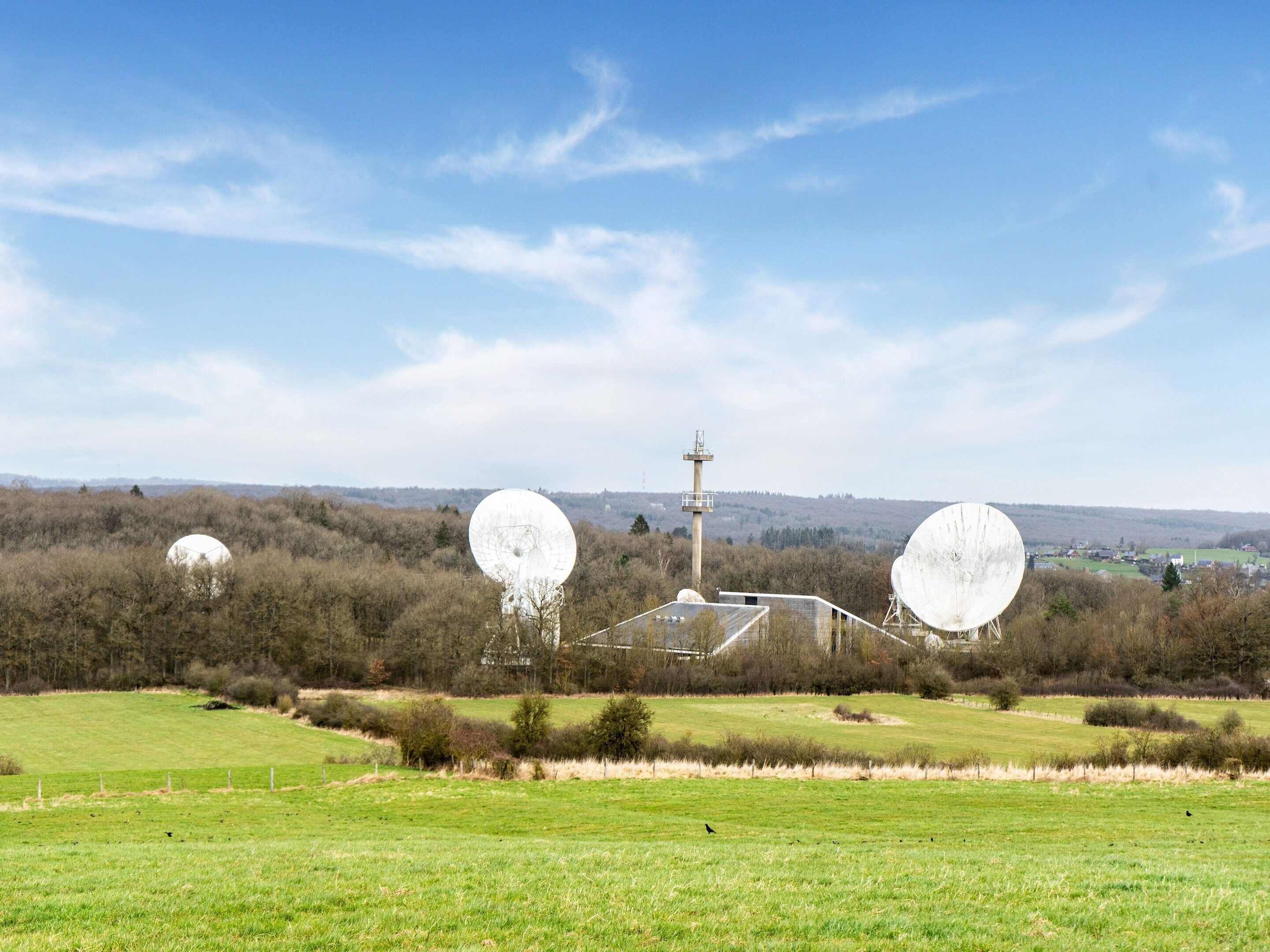 A rural landscape with three large satellite dishes and a communication tower.