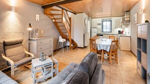 A cozy living room with a sofa, a small table, a chair, a staircase, and a kitchen area with a dining table and chairs. - Cottage With Garden, Lessive (Rochefort)