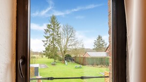 A view through a window of a backyard with a wooden fence, a picnic table, a bench, and a slide. - Cottage With Garden, Lessive (Rochefort)