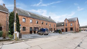 A brick building with a gravel driveway, two parked vans, and a utility pole. - Cottage With Garden, Lessive (Rochefort)