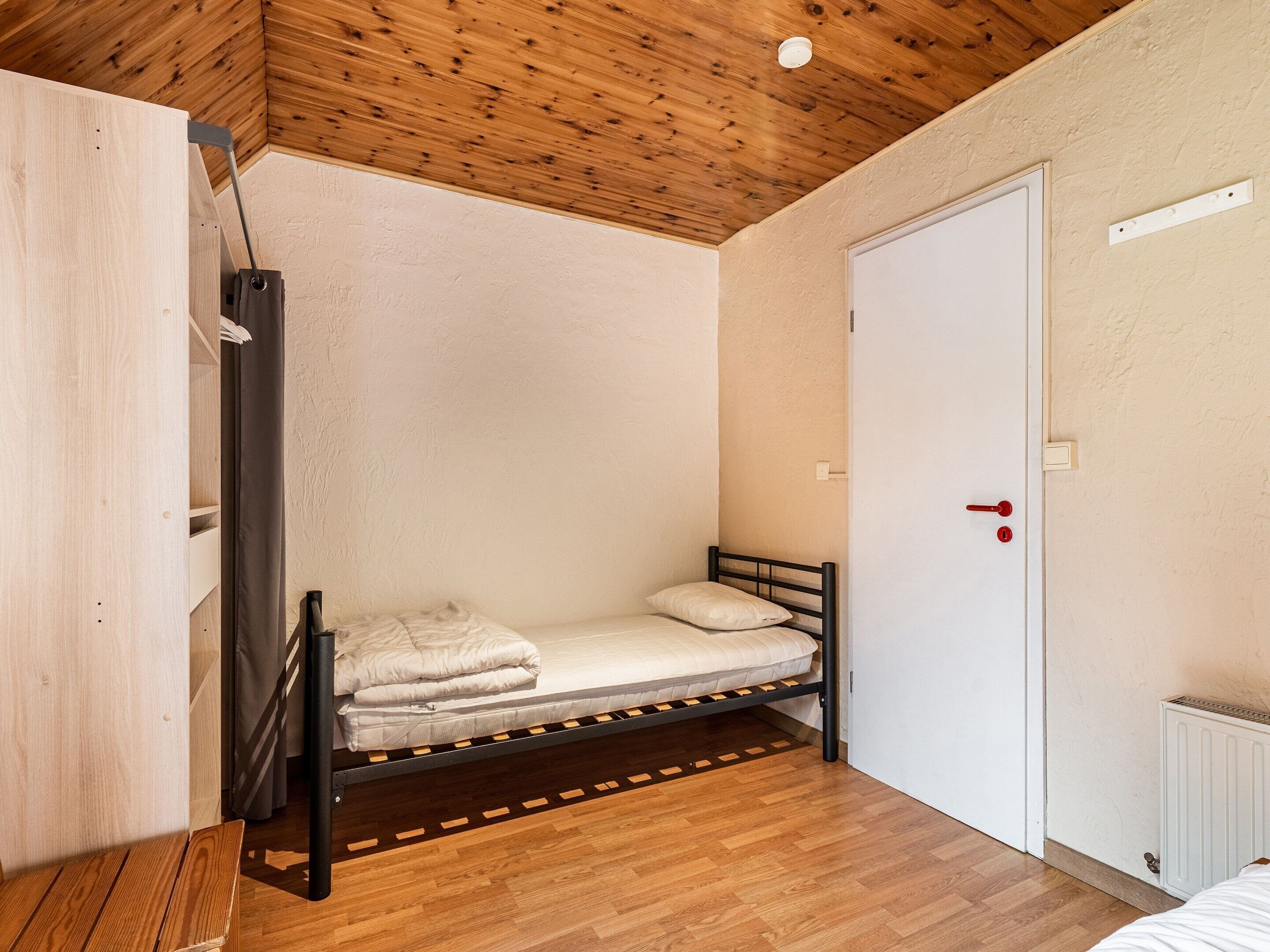 Una habitación pequeña con cama individual, techo de madera, puerta blanca y radiador.