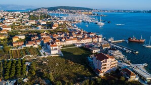 Vista aérea de uma cidade costeira com um porto de iates, edifícios residenciais e um grande edifício branco com uma torre.