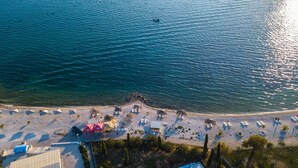 Vista aérea de uma praia com espreguiçadeiras, guarda-sóis e um pequeno barco na água.