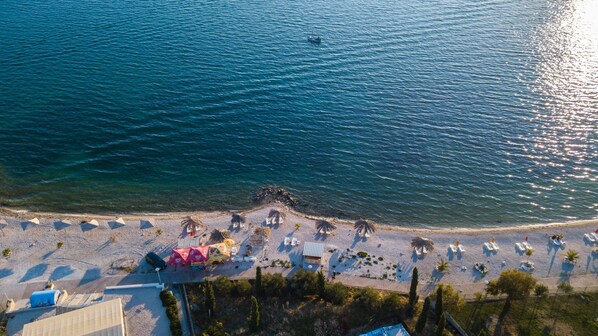 An aerial view of a beach with sun loungers, umbrellas, and a small boat in the water.
