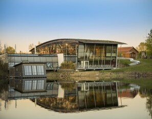 A modern building with a glass facade, a reflection in the water, and a small adjacent structure. - Small Apartment in Hesse With Terrace and Garden (Frielendorf)