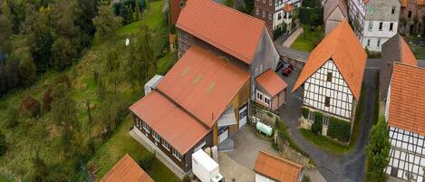 An aerial view of a village with traditional half-timbered houses, a large building with a red roof, and a truck parked in front.