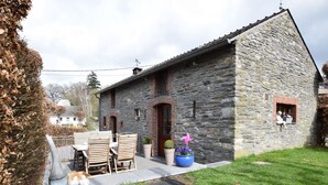 Un bâtiment en pierre doté d’une terrasse, d’une table et de chaises.