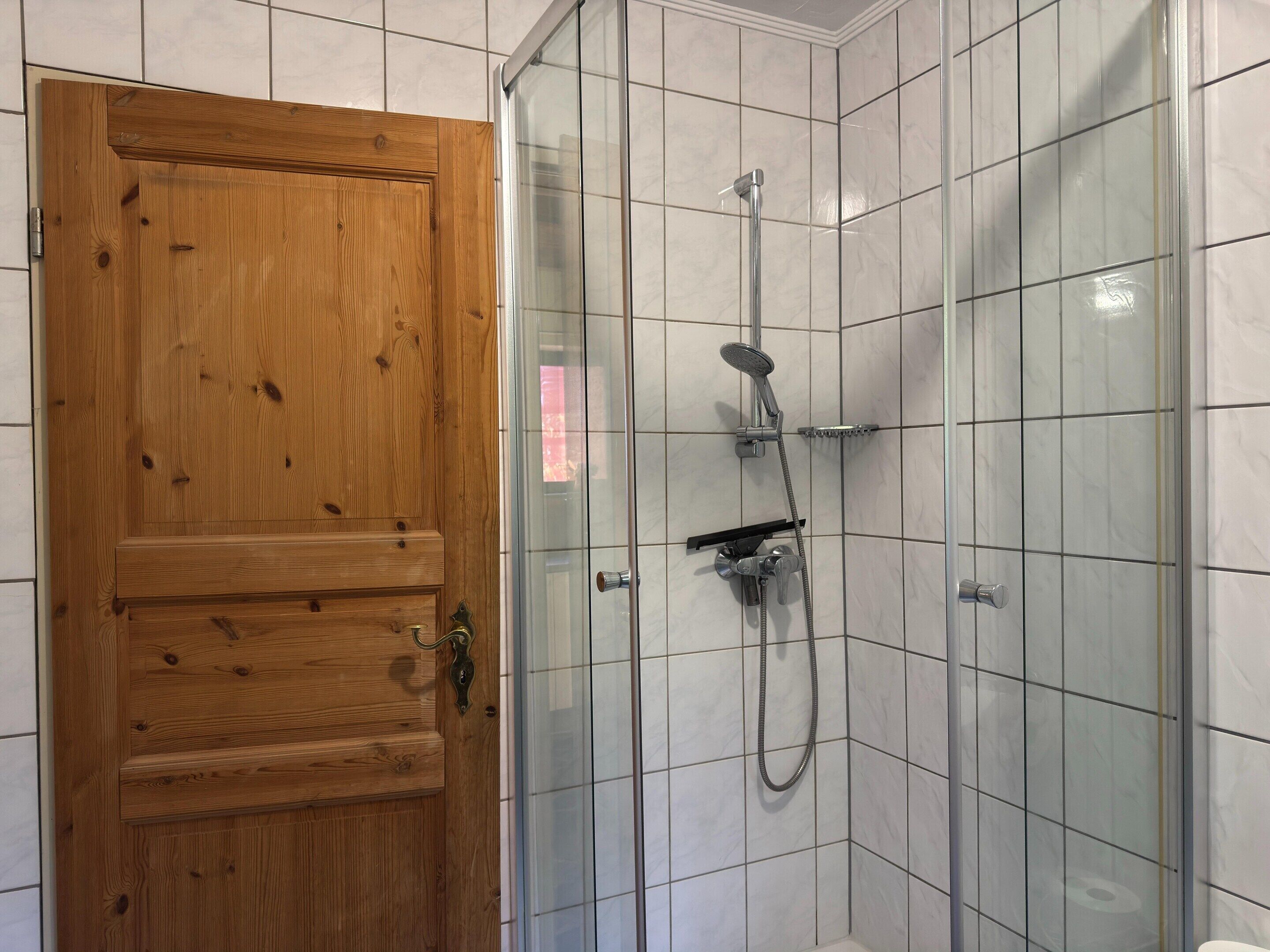 A shower with a glass door, a wooden door, and tiled walls.