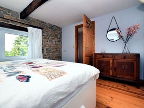 A bedroom with a bed, a wooden dresser, a stone wall, a window with curtains, and a mirror on the wall. - Vintage Holiday Home in Durbuy With Terrace, Garden, Parking (Durbuy)