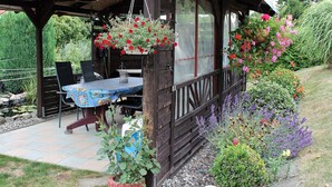 Een houten pergola met een tafel en stoelen eronder, omgeven door een tuin met verschillende planten en bloemen.