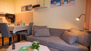 Een woonkamer met een bank, een eettafel met stoelen, een keuken en een wandplank met decoratieve objecten.