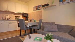 Een compact woongedeelte met een kitchenette, een eethoek en een bank met kussens.
