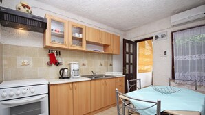 A compact kitchen with wooden cabinets, a white stove, and a dining table with a blue tablecloth. - Holiday Apartment Medulin 1 - Elena (Medulin)