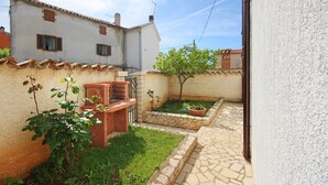 A courtyard with a small garden, a wooden bench, and a brick wall. - Holiday Apartment Medulin 1 - Elena (Medulin)