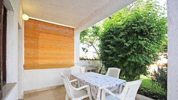 An outdoor patio with a table and chairs, a window with blinds, and a large green bush. - Holiday Apartment Medulin 1 - Elena (Medulin)