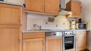 A modern kitchen with wooden cabinets, a stainless steel sink, a built-in oven, and a microwave.