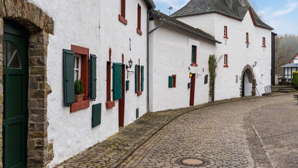 A traditional building with a cobblestone street, stone foundation, and green shutters.
