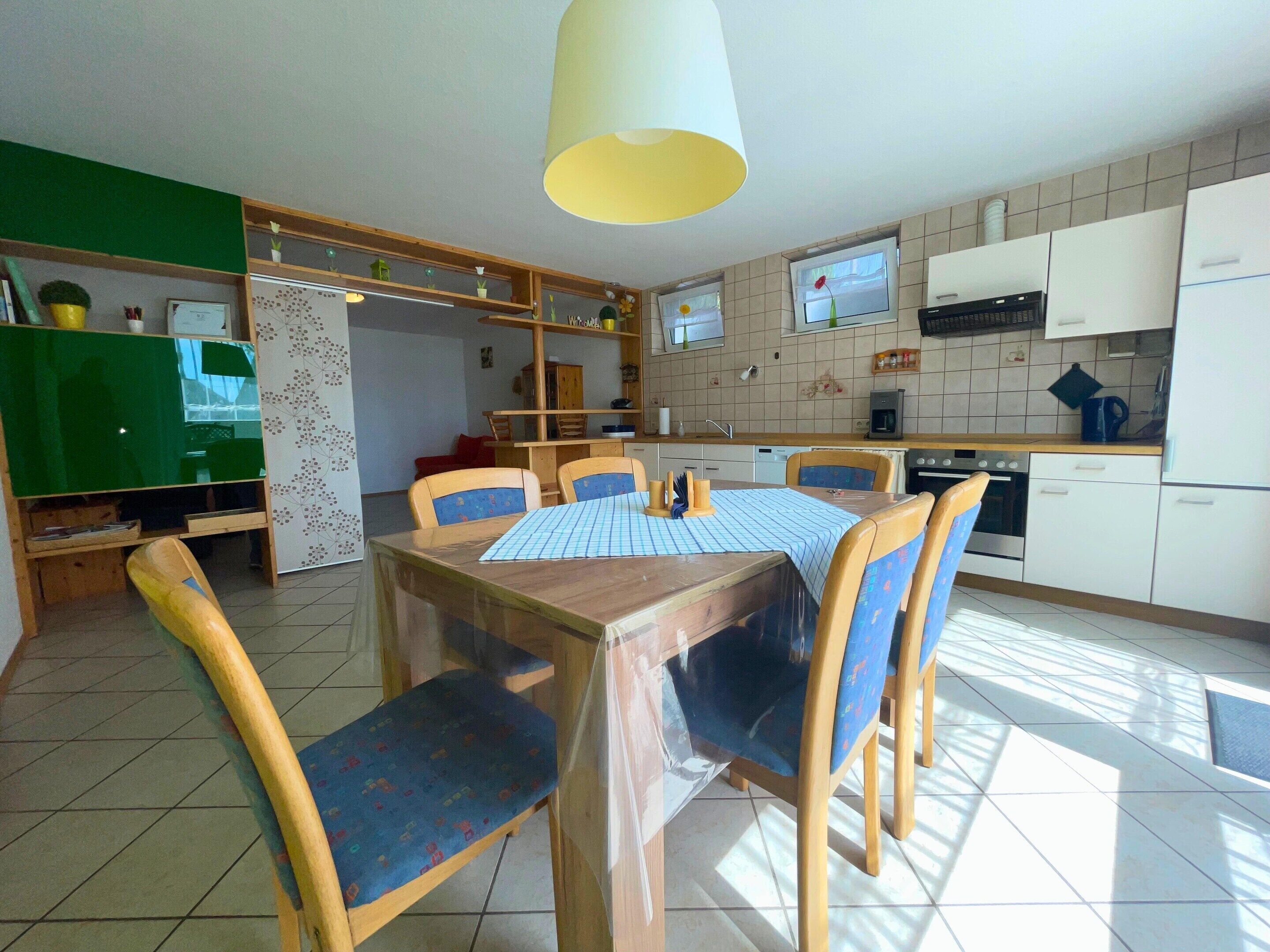 A compact kitchen with a dining area, featuring a table with chairs, a ceiling light, and a view of the adjacent living area.