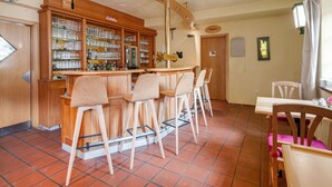 Una zona de bar con mostrador de madera, varios taburetes y un reloj en la pared.