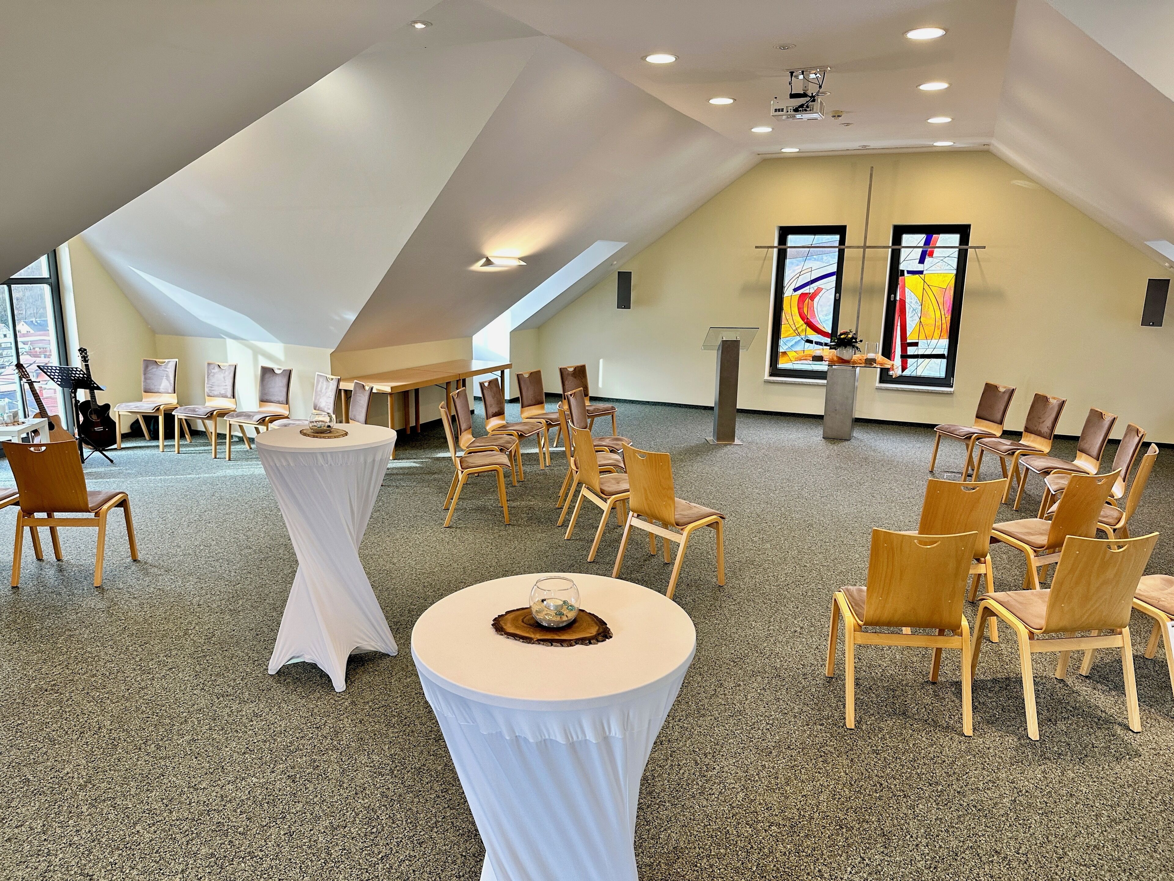 Een ruime vergaderzaal met hoge plafonds, een podium en een groot raam met abstracte kunst.