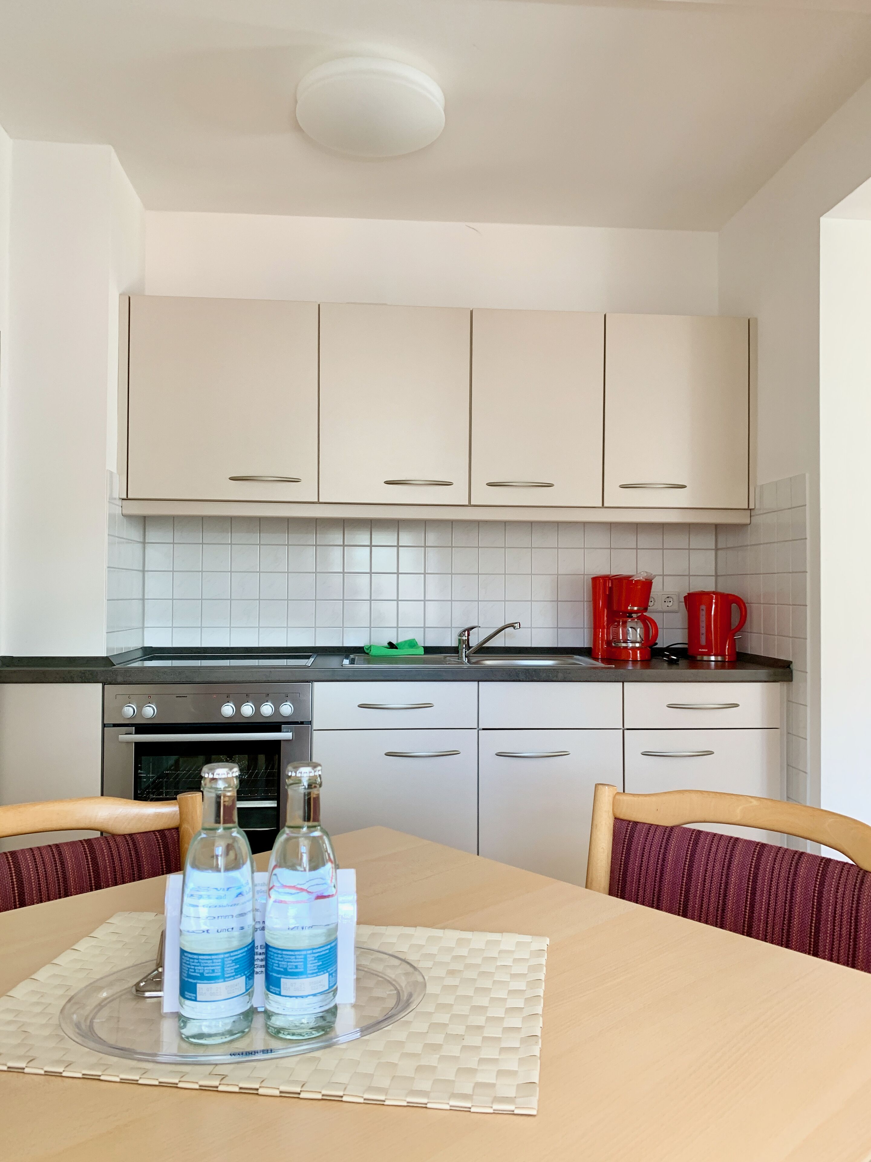 Una cocina con armarios blancos, encimera negra y una mesa de comedor con dos botellas de agua.
