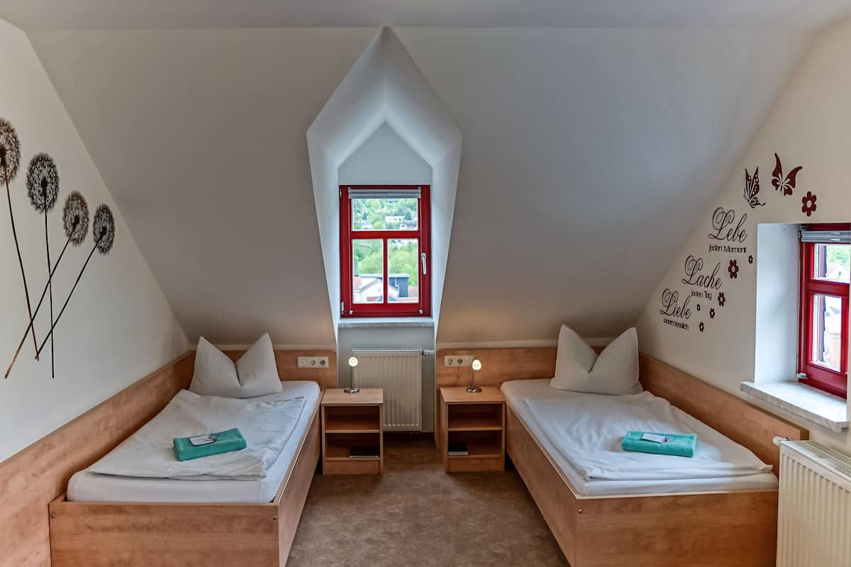 A bedroom with two beds, a window, a radiator, and wall decorations.
