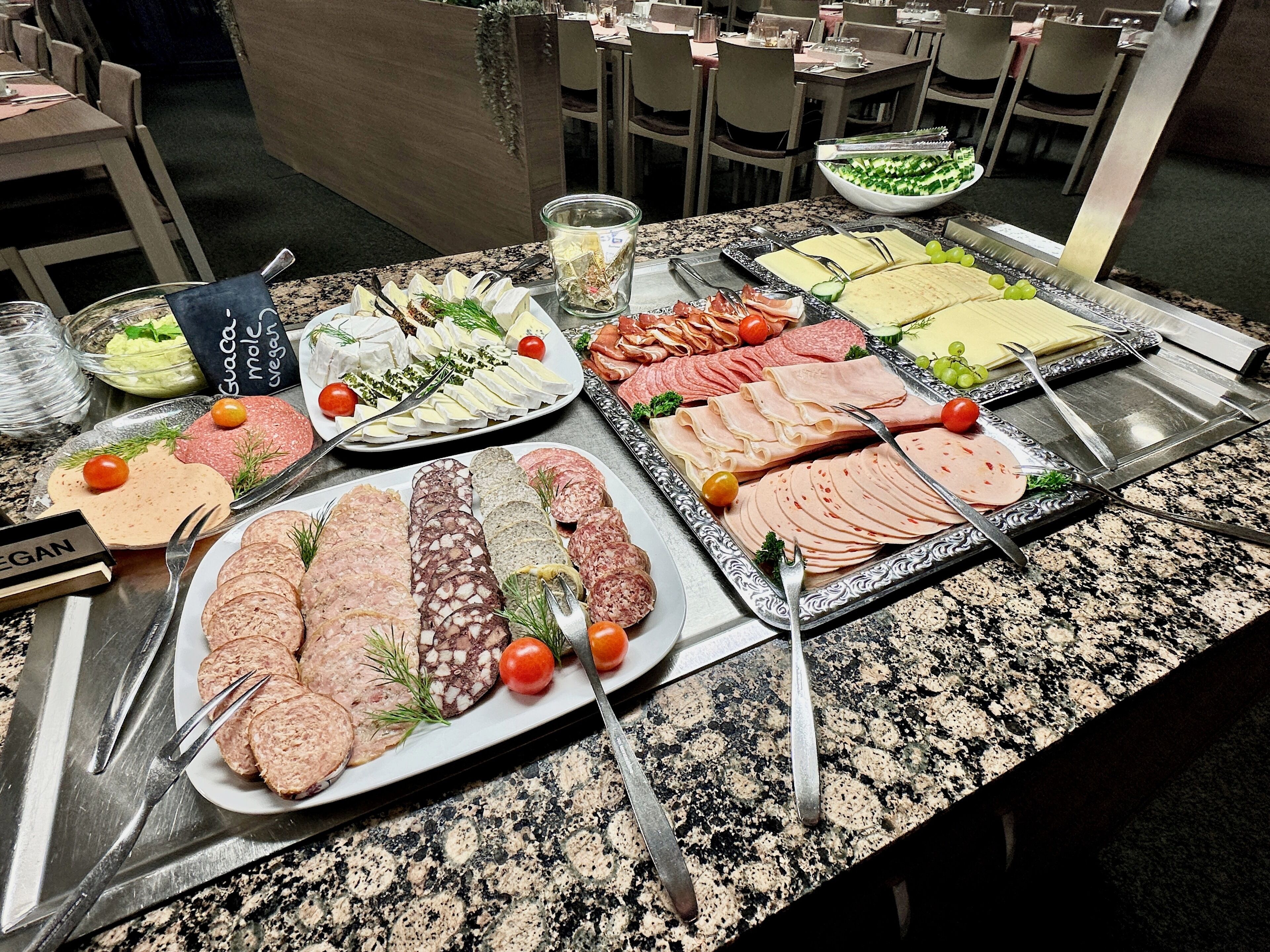 A buffet table with various food items, including meats, cheeses, and vegetables, arranged on plates and serving trays.