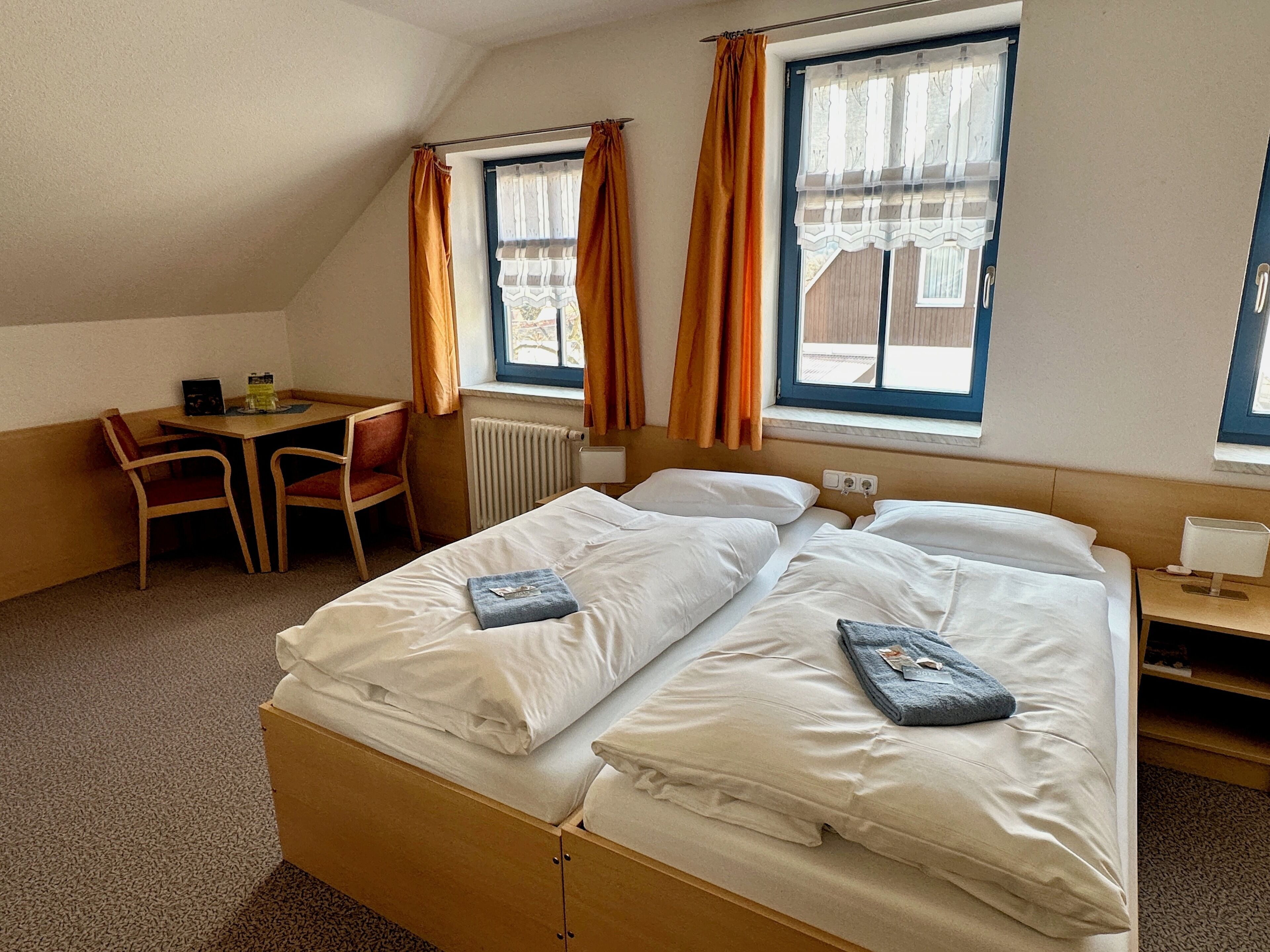 Quarto de hotel com duas camas, uma mesa e uma cadeira.