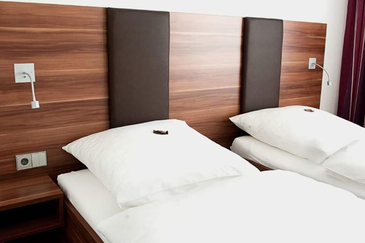 A hotel room with a wooden headboard, two beds with white bedding, a nightstand, and a power outlet.