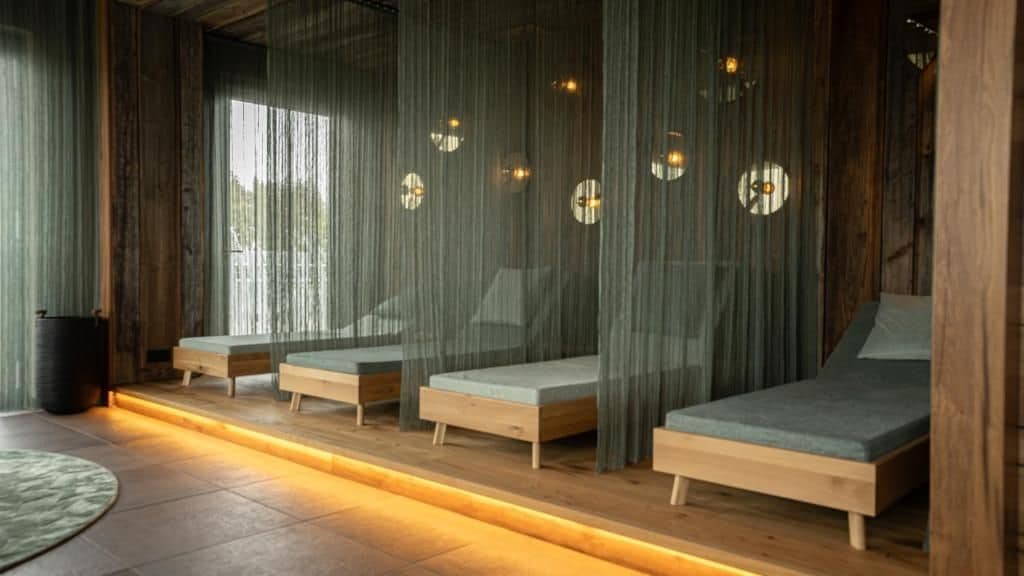 Una habitación con varias camas dispuestas junto a la pared, cortinas traslúcidas, una mesita redonda y un cubo de basura.