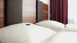 A hotel room with two beds, a wooden headboard, and a window with curtains. - Hotel Sentio (Voehringen)