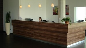 A reception desk with a wooden finish, three pendant lights, a large potted plant, and a painting on the wall. - Hotel Sentio (Voehringen)