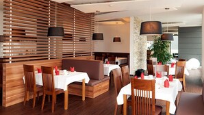 A modern restaurant with wooden slatted walls, white tables, and brown cushioned seating. - Hotel Sentio (Voehringen)