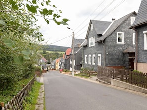 En smal gata kantad av traditionella hus, ett trästaket och fri sikt över vägen framför.