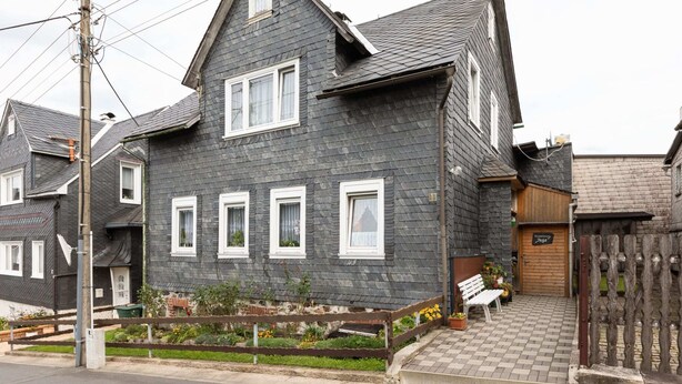 A two-story house with a dark grey exterior, white window frames, and a wooden front door.